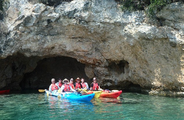 people doing Kayak on the beach of Epidaurus in front of a cave